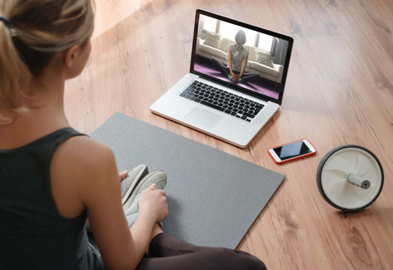Yoga teacher conducting virtual class at home on a video conference. Young beautiful woman doing an online yoga class in her living room with laptop. Home fitness and workout concept