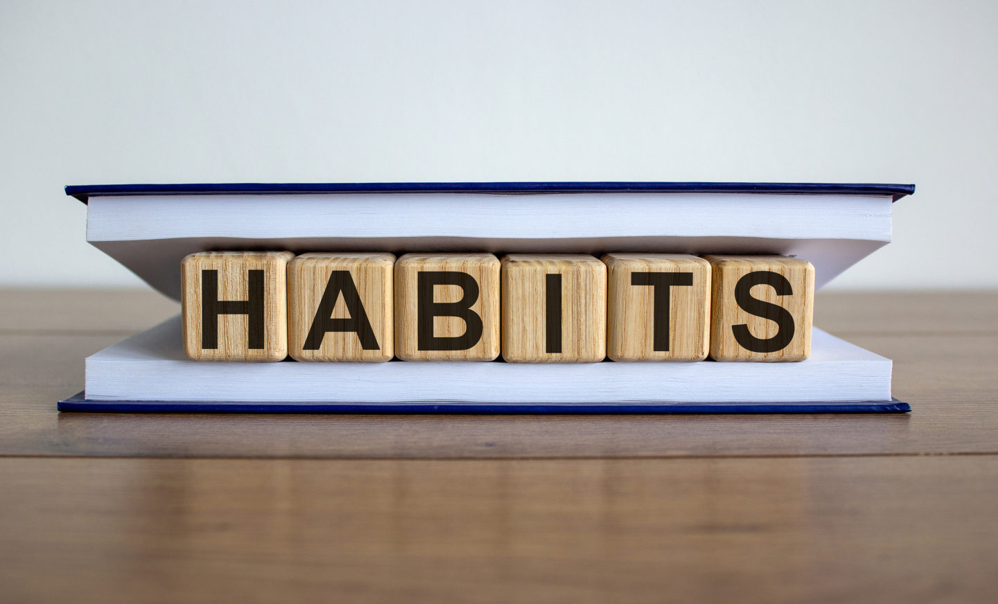 Concept word 'habits' on wooden cubes between pages of a book on a beautiful wooden table. White background. Business concept.