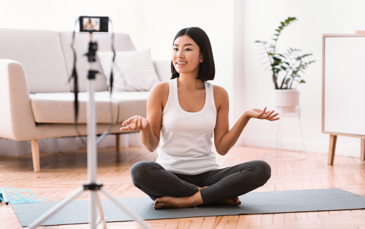 Fitness Vlog. Portrait of active asian woman filming video for her internet channel at social media, looking and talking to camera, sitting on the floor on yoga mat. Trainer recording tutorial at home