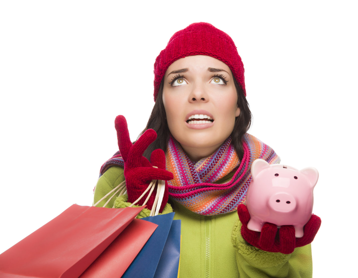 Stressed Mixed Race Woman Wearing Winter Clothing Looking Up Holding Shopping Bags and Piggy Bank Isolated on White Background.