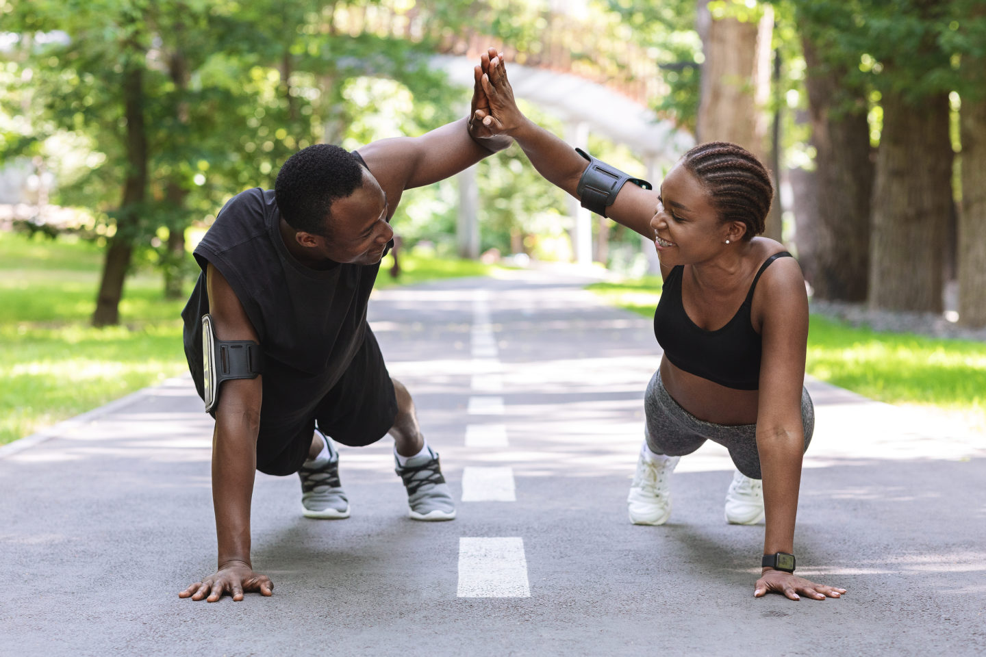 Motivated couple giving high-five to each other while working out outdoors, standing in plank or doing push ups in park, clapping hands