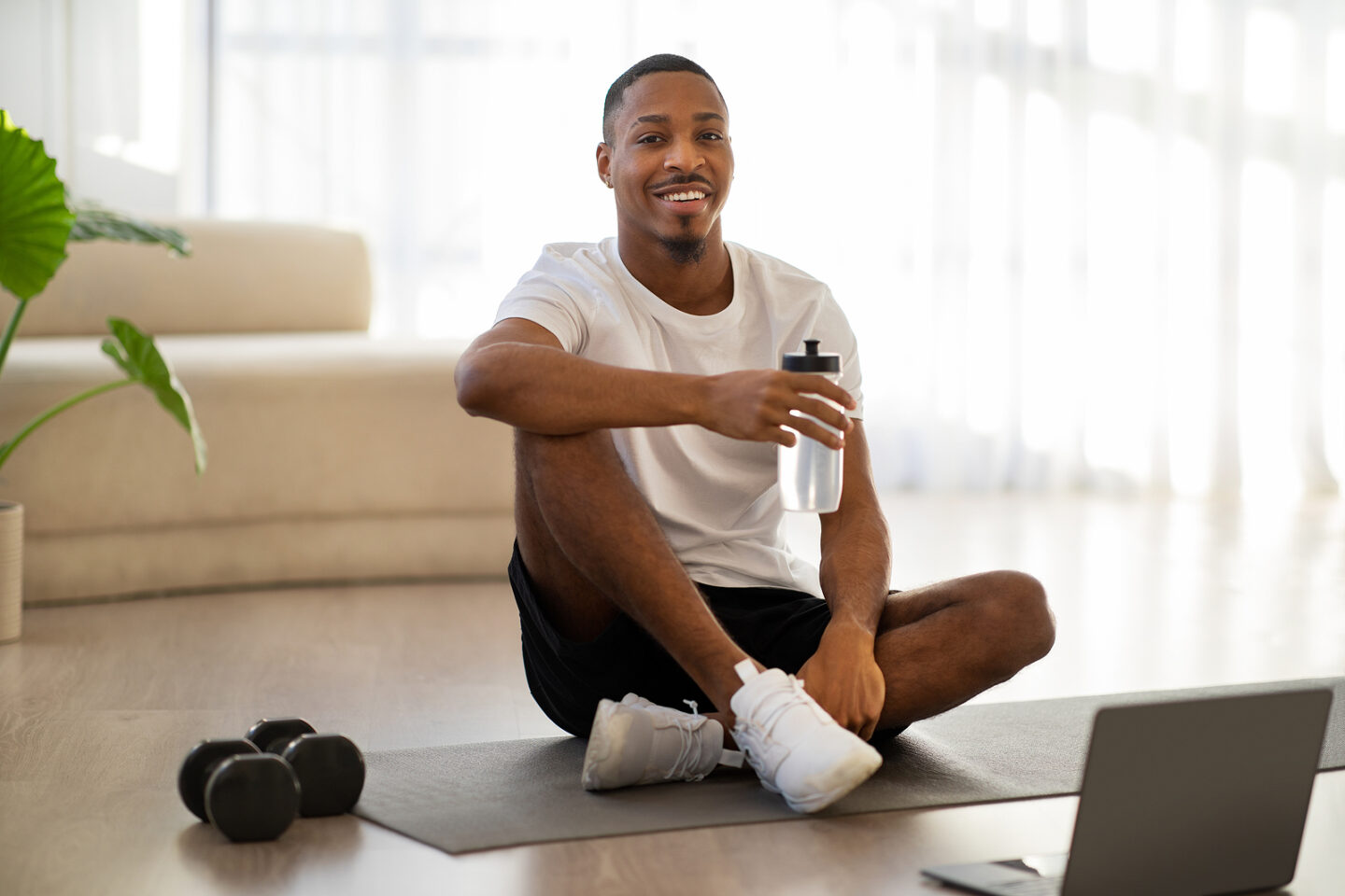 Cheerful black guy drinking water after workout online at home